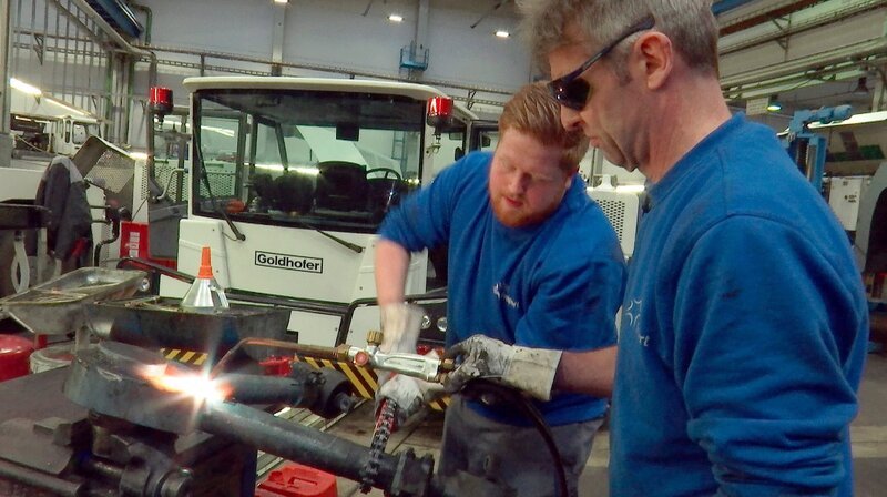 Robert Schammbach und Fabian Hartmann sind KFZ-Mechatroniker in der Fuhrparkwerkstatt am Frankfurter Flughafen, der größte Spezialwerkstatt der Welt. – Bild: HR