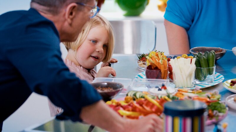 Mehr Gesundes für die Kita-Box: Mittags isst Lotta im Kindergarten. Matthias Riedl zeigt ihr, was für sie gut ist. Und die Vierjährige mag tatsächlich vieles von dem vorgeschnittenen Gemüse. – Bild: NDR/​Oliver Zydek
