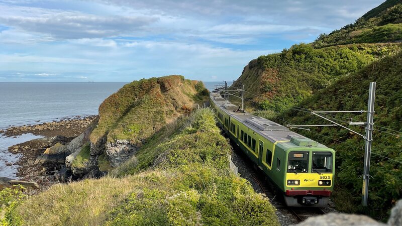 Der DART lässt die letzte Klippe hinter sich liegen: Der Nahverkehrszug zwischen Greystones und Bray fährt auf eingleisiger Strecke. Parallel zur Bahn verläuft ein Spazierweg, der Cliff Walk. – Bild: ZDF und SWR/​Kirsten Ruppel