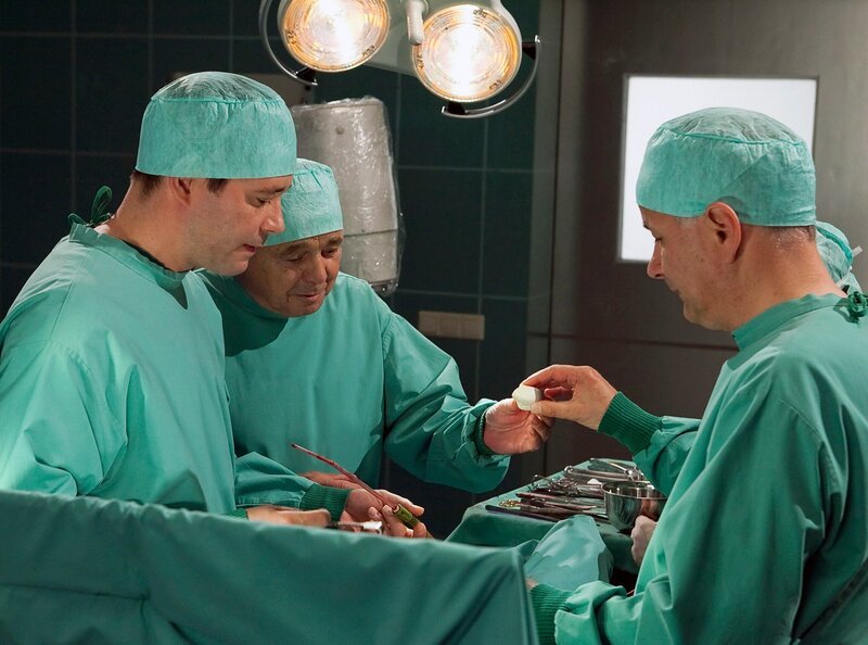 Als Dr. Roland Heilmann (Thomas Rühmann, rechts) und Dr. Philipp Brentano (Thomas Koch, links) das erste künstliche Knochenimplantat bei einer Probandin einsetzen, kommt sogar Prof. Simoni (Dieter Bellmann) wissbegierig in den OP. – Bild: MDR/​MDR/​Saxonia/​Krajewsky