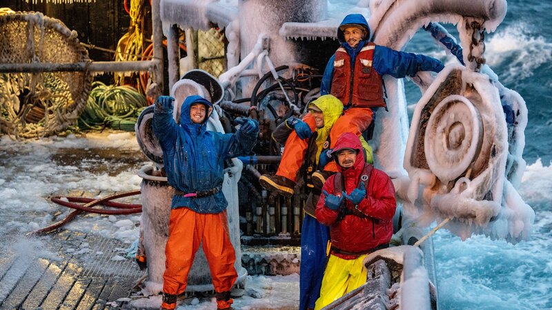 Blickwinkel vom Steuerhaus aus, die Wizard-Crew auf dem kalten, vereisten Deck lächelt und winkt in Richtung Kamera. – Bild: Warner Bros. Discovery, Inc. or its subsidiaries and affiliates.