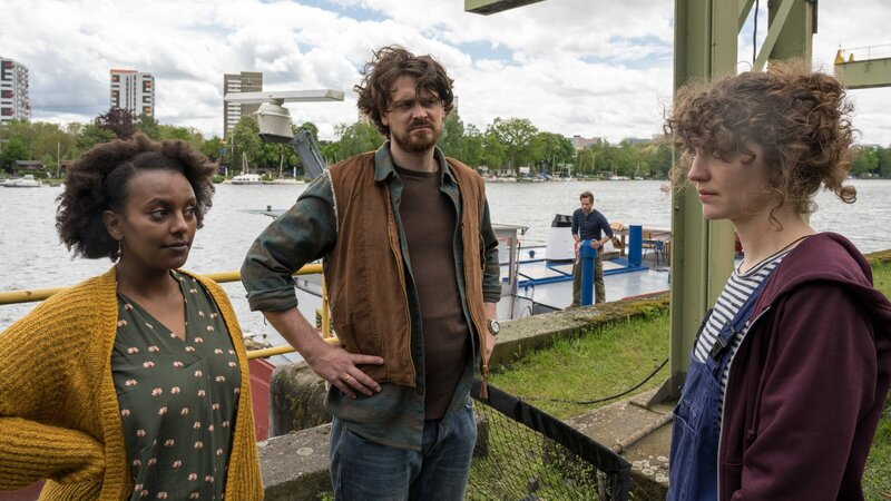 Skeptische Blicke: Sabine (Yodit Tarikwa, l.) und Hanno Pfeiffer (Sebastian Fräsdorf, 2.v.l.) sind zwar froh, Noraly van de Wal (Anne Rietmeijer, r.) wieder an Bord zu haben, aber trotzdem haben sie einige Fragen. Im Hintergrund steht Leo Oswald (Wanja Mues, 2.v.r.), der an Deck der „Zora“ arbeitet und die Gruppe beobachtet. – Bild: ZDF