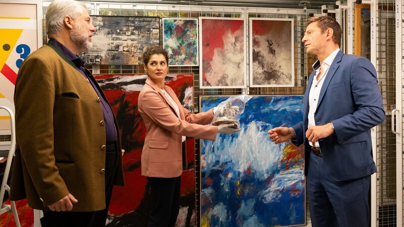 Rechtsmedizinerin Dr. Dimos (Anastasia Papadopoulou, M.) informiert die Kommissare Stadler (Dieter Fischer, l.) und Hansen (Igor Jeftić, r.), dass das Mordopfer von hinten mit einer Plastik der Gottheit Shiva erschlagen wurde. – Bild: ZDF und Linda Gschwentner