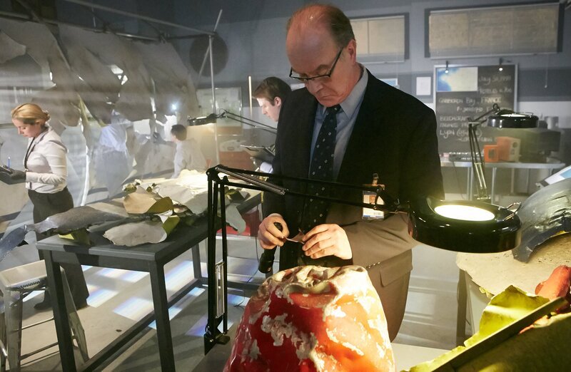 RE-ENACTMENT – Bouillard (played by Stuart Clow) inspects the red painted pieces of the crash. Investigators (played by background performers) take notes in the background. – Bild: National Geographic Channel