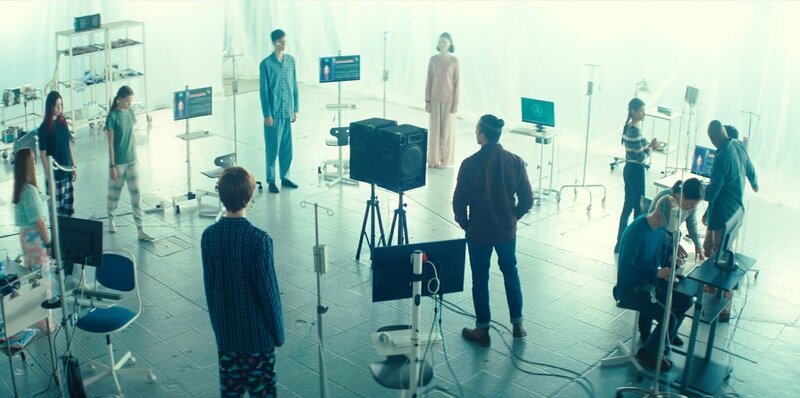 In einem Schlaflabor untersucht „Greenfront“ – u.a. Fischer (Fayez Bakhsh, 7.v.l.) und Charlotte (Frances Mayli Mccann, 3.v.r.) – die Jugendlichen – Meg (Katy Byrne, l.), Kaz (Maiya Silveston, 2.v.l.) und Luka (Pádraig McCormack, 4.v.l.) – die wie Schlafwandler nachts hineingeströmt sind. Monika (Lucy Chambers, 3.v.l.), Louis (Oliver Cunliffe, 5.v.l.), Isabel (Alis Waters, 6.v.l.) haben sich bereits zu ihnen mit in den Kreis gestellt, während Glen (Krish Misra, r. verdeckt) von einem „Greenfront“-Mitarbeiter zum Kreis geführt wird. – Bild: ZDF/​Zodiak Kids & Family Productions UK Ltd.