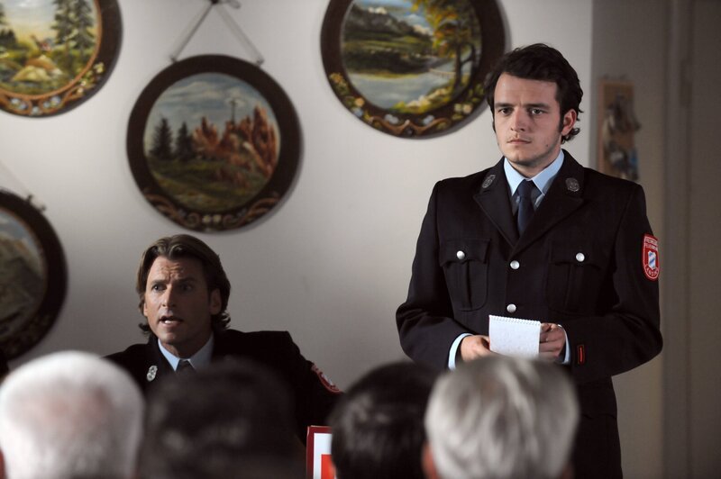 Flori hält eine Rede zur Jugendförderung bei der Feuerwehr. Von links: Sebastian Wildner (Herbert Ulrich) und Florian Brunner (Tommy Schwimmer). – Bild: BR/​Marco Orlando Pichler