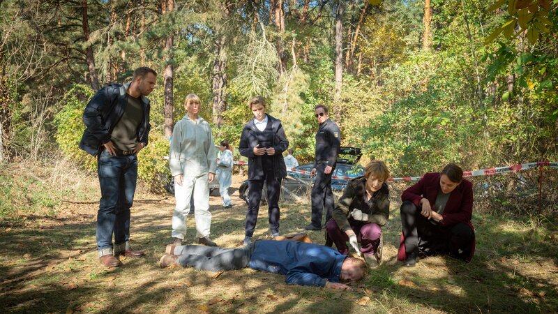 Gabriel Faber (Tobias von Heymann, liegend) liegt tot im Wald. Das Team der SOKO Wismar (v.l.n.r.: Lars Pöhlmann (Dominic Boeer), Roswitha Prinzler (Silke Matthias), Stine Bergendal (Sidsel Hindhede), Kai Timmermann (Mathias Junge), Dr. Helene Sturbeck (Katharina Blaschke), und Karoline Joost (Nike Fuhrmann) wundert sich: Was hat der Schiffsmechaniker hier in Wismar gewollt? Zuletzt ist Faber noch in Norwegen und Fernost unterwegs gewesen … – Bild: ZDF und Marc Meyerbröker