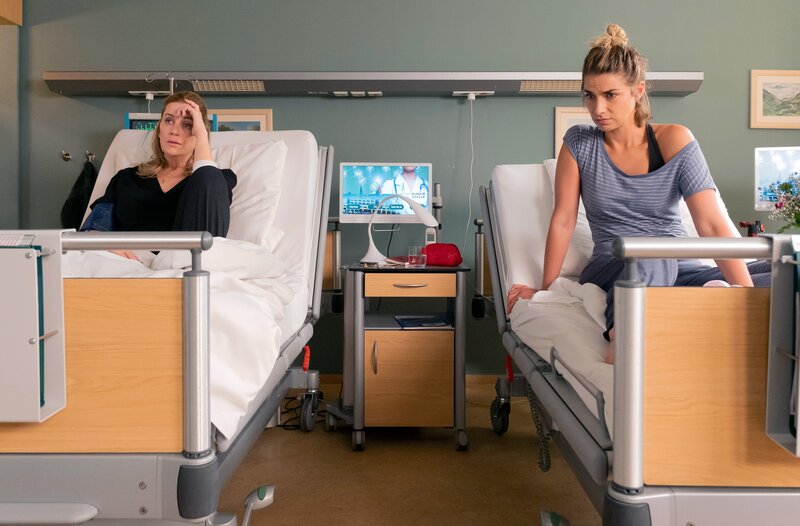 Bea Hölsch (Daniela Wutte, re.) ist mit Fieber umgekippt und hat sich einen Schlüsselbeinbruch zugezogen. Ihren behandelnden Arzt Dr. Martin Stein (Bernhard Bettermann, li.) bringt sie mit ihrem sehr anschmachtenden Verhalten in eine ziemlich unangenehme Situation. Auch Dr. Kathrin Globisch (Andrea Kathrin Loewig, mi.) ist ziemlich irritiert. – Bild: MDR/​Saxonia Media/​Sebastian Kiss