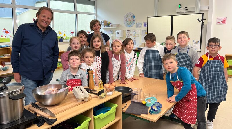 Björn Freitag (l) bereitet gemeinsam mit Lehrerin Malaika Noss (hinten, 2.v.l.) und den Kindern der Koch-AG einfache Kindergerichte zu. – Bild: WDR/​solis TV/​Joshua Stolz