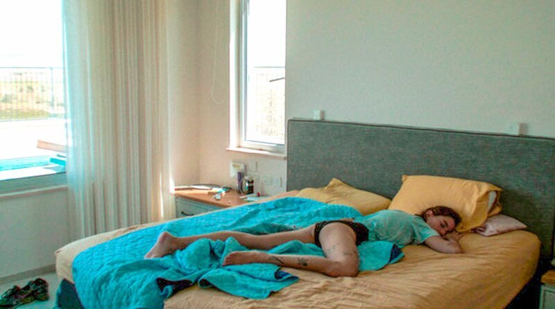 Die spontan zu Besuch gekommene Romi (Levi Yuval) holt den auf einem Rave verpassten Schlaf nach. – Bild: NDR/​Schuldenberg Films/​Median Arama