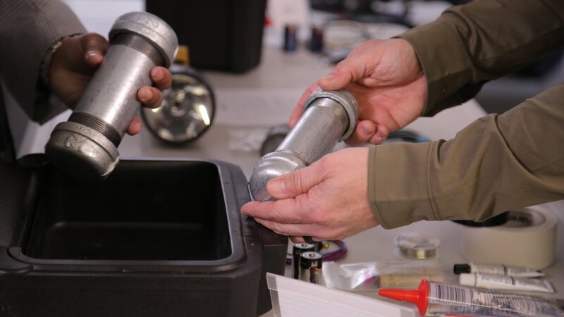 Bomb expert Richard Campbell and Chris Anderson hold pieces of household items that can be used to make bombs in an office demonstration. – Bild: Discovery Communications, LLC