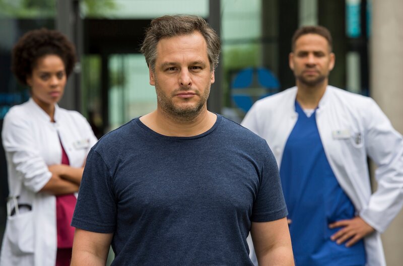 Piet (Sebastian Nakajew, M.) stößt Matteo (Mike Adler, h.r.) und Vivi (Jane Chirwa, h.l.) vor den Kopf, als er ihre Behandlung ablehnt. – Bild: ARD/​Jens-Ulrich Koch