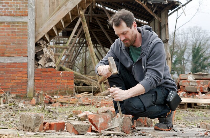 Stephen Warneyer beim Backsteine zerkleinern. – Bild: NDR/​Reinhard Bettauer