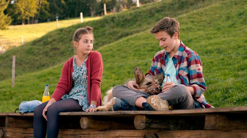 Fee (Joline Letizia Schwärzler) und Flori (Lino de Greiff) suchen nach einem Plan und wollen Racko (Chewakka) vom Maulkorb befreien. – Bild: BR/​Filmbüro Münchner Freiheit GmbH