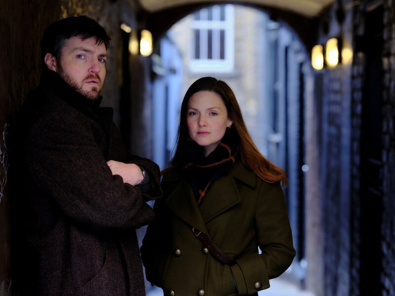 l-r: Tom Burke als Cormoran Blue Strike, Holliday Grainger als Robin Venetia Ellacott – Bild: Laurence Cendrowicz/​HBO /​ Warner
