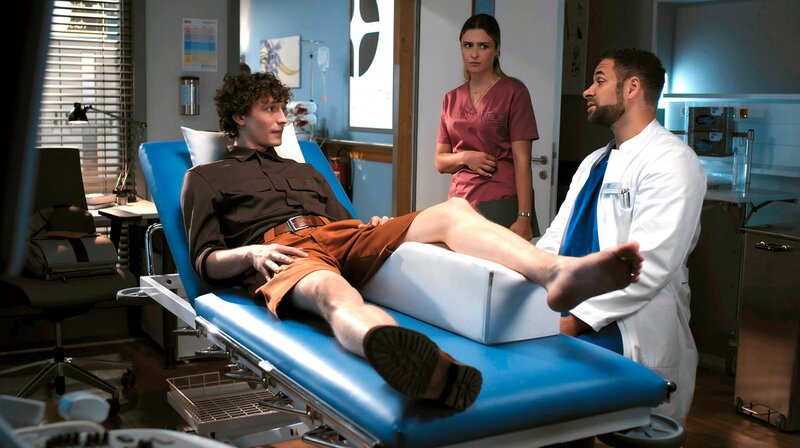 Dr. Matteo Moreau (MIke Adler, r.) will dem Kurier Malte Severins (Jonathan Lade, l.) das Päckchen abnehmen. Doch Viktoria Stadler (Isabella Krieger, M.) will den auffällig humpelnden jungen Mann nicht gehen lassen. – Bild: ARD/​Jens-Ulrich Koch