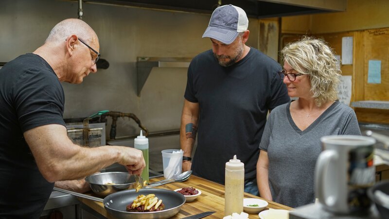 Chef Robert Irvine shows Leah Fogle & Chris Fogle, Leah’s Korner Kafe, how to make the entrées from the new menu at Leah’s Korner Kafe in Coleman, MI, as seen on Restaurant: Impossible Season 20. – Bild: Food Network – US /​ Lando Entertainment, LLC /​ © 2022, Discovery, Inc. All Rights Reserved.