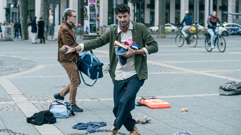 Für sein Kunstprojekt, verstreut der Künstler Schuhe und Taschen auf einem städtischen Platz: Juan Lo Sasso als Amadeo Reyes (vorne) – Bild: SRF/​ZDF/​Daniel Dornhöfer