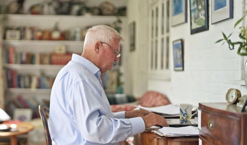 Eine Person sitzt an einem Schreibtisch in häuslicher Umgebung und arbeitet mit Unterlagen. – Bild: Crime + Investigation /​ Sarah Rest