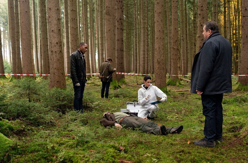 Dr. Bitterling (Genoveva Mayer, 2.v.r.) untersucht die Leiche, während die Kommissare Beissl (Andreas Giebel, r.) und Jerry Paulsen (Peter Marton, l.) sich am Tatort umsehen (mit Siegfried Terpoorten, h.). Weiteres Bildmaterial finden Sie unter www.br-foto.de. – Bild: ARD/​Lucky Bird Pictures/​Angela M. Schlabitz