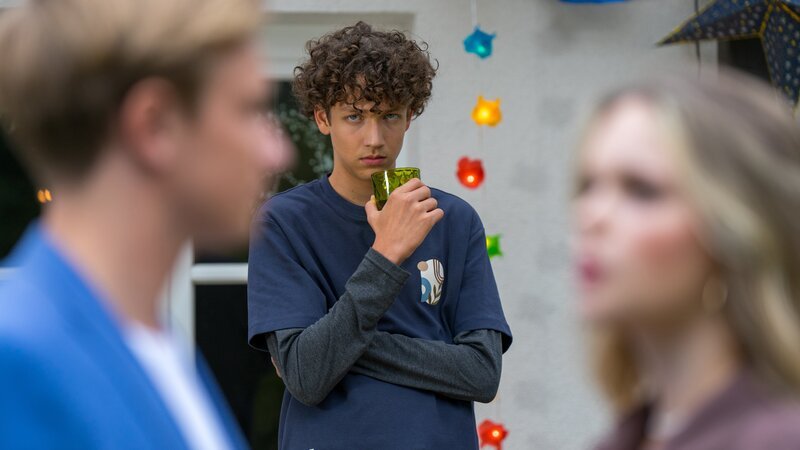 Edvard (Levi Kazmaier) beobachtet, wie Jason (Christian Kemme) auf der Party mit Constanze (Celina Gehringer) spricht. – Bild: SWR/​2023 Mingamedia/​Daniel Klare