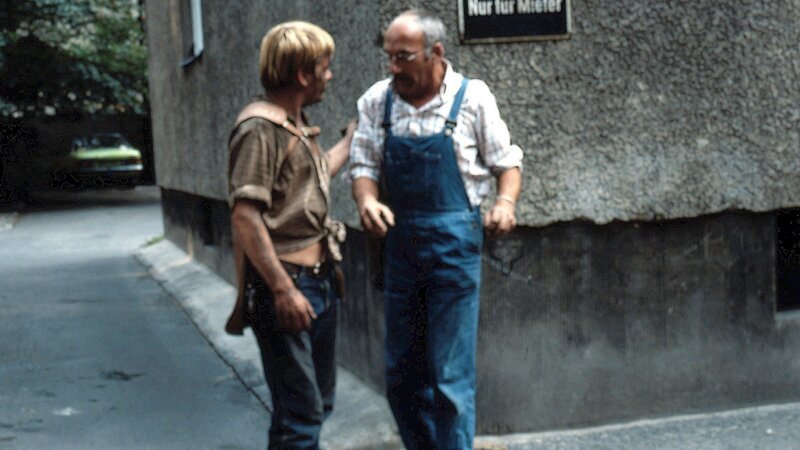 Peter Lustig (r.) ist über einem Kohlestückchen auf dem Bürgersteig ausgerutscht. Irritiert und verwundert über die herumliegende Kohle, spricht er den „Kohlemann“(l.) an. Dieser hat aber nur wenig Verständnis für Peters Fragerei. – Bild: ZDF und Studio-TV