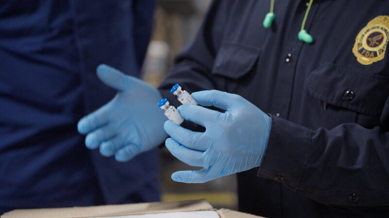 Ein FDA-Beamter hält zwei Fläschchen mit möglicherweise gefälschtem Botox in der Hand und untersucht sie. Die Fläschchen wurden in einer Lieferung gefunden. – Bild: National Geographic/​Lucky 8 TV /​ National Geographic