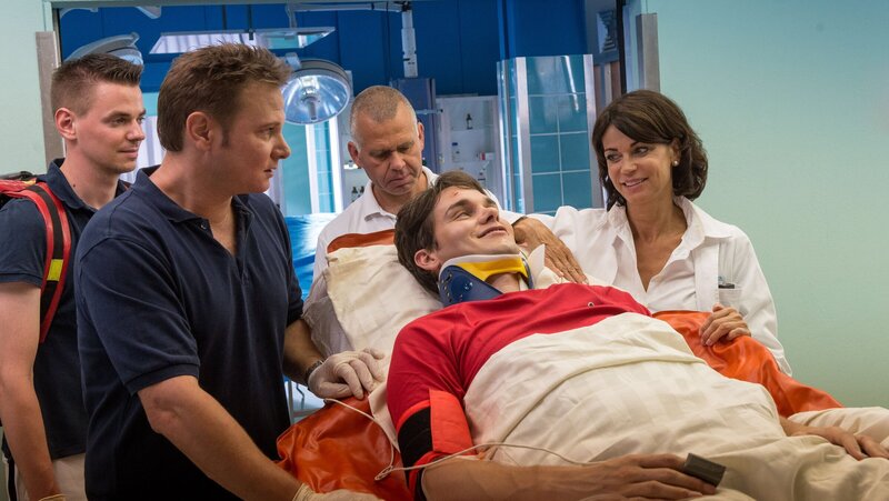 Dr. Haase (Fabian Harloff, 2.v.l.) liefert den Stabhochspringer Josh Baier (Daniel Fünffrock, 2.v.r.) ins EKH ein. Der junge Sportler kann es selbst nach seinem Unfall nicht lassen, mit Jasmin (Gerit Kling, r.) zu flirten. – Bild: ZDF