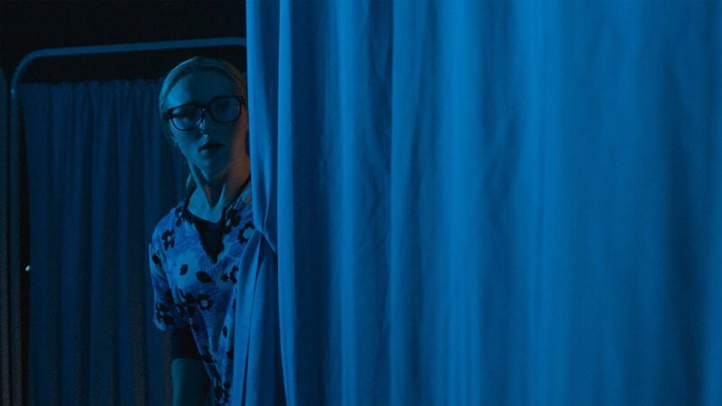 A frightened nurse looks behind the curtain. – Bild: Blue Ant Media