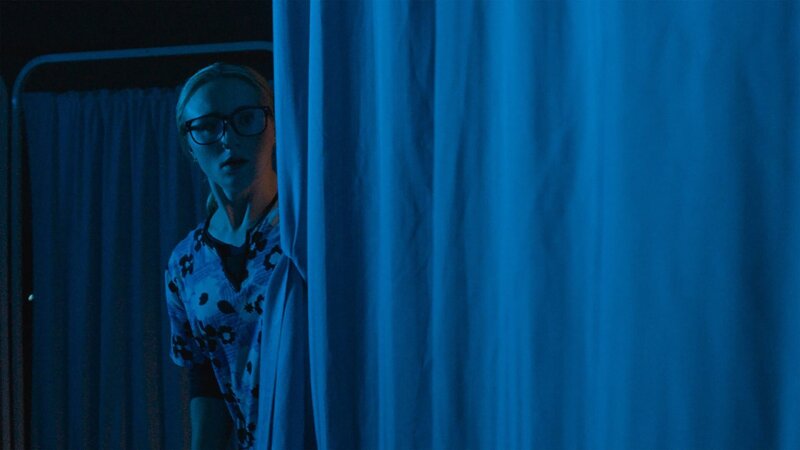 A frightened nurse looks behind the curtain. – Bild: Blue Ant Media