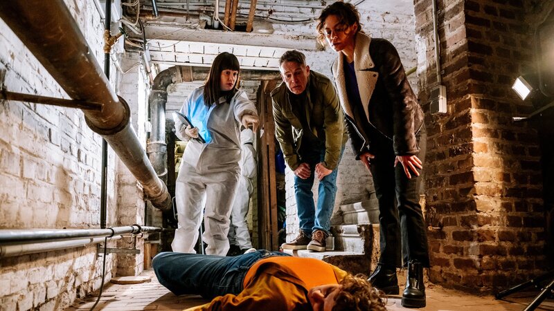 Valeria Greco (Sophie Killer, liegend) wird tot an der Kellertreppe ihrer Wohnung gefunden. Doch wie Dr. Westphal (Yulia Yáñez Schmidt, l.) den Kommissaren Matti Wagner (Pierre Besson, M.) und Lilly Funke (Tatjana Kästel, r.) berichtet, muss sie jemand mit böser Absicht ermordet haben, denn sie wurde vorher schon erstickt. – Bild: ZDF und Martin Rottenkolber