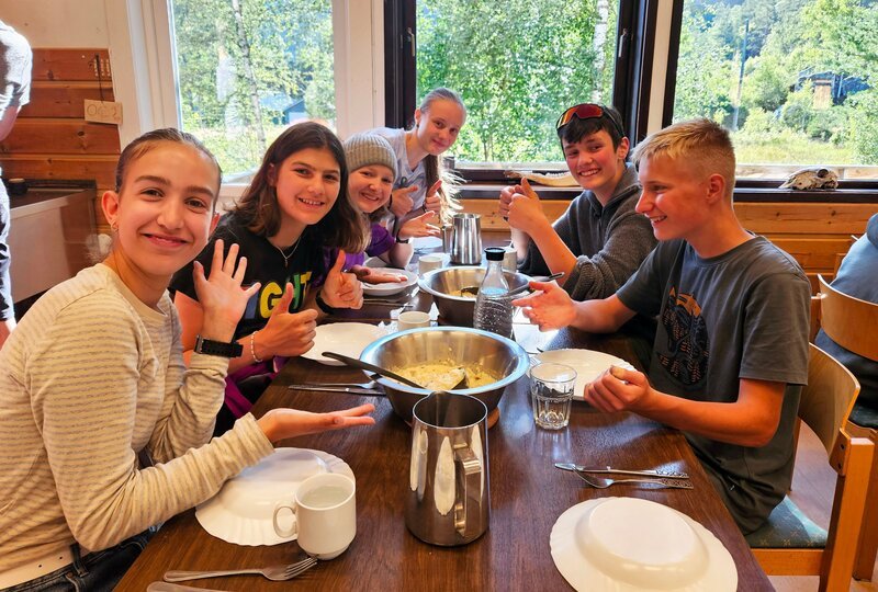 Geschafft! Emmas und Maxis erster Einsatz im Küchenteam ist erfolgreich. Risotto mit leicht angebrannter Note? Check! Von links: Emma, Emilia, Leyla, Kaja, Max und Maxi lassen es sich schmecken. – Bild: Megan Ehrmann /​ BR /​ Bewegte Zeiten Filmproduktion GmbH