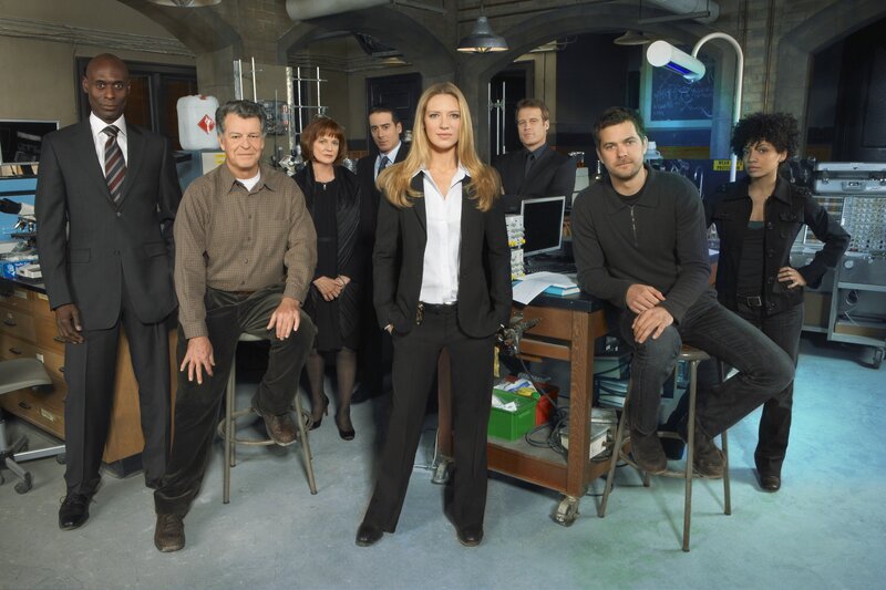 v.l.n.r.: Phillip Broyles (Lance Reddick), Dr. Walter Bishop (John Noble), Nina Sharp (Blair Brown), Charlie Francis (Kirk Acevedo), Olivia Dunham (Anna Torv), John Scott (Mark Valley), Peter Bishop (Joshua Jackson) und Astrid Farnsworth (Jasika Nicole) – Bild: Warner TV Serie