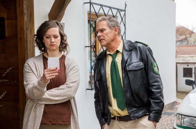 Mara Beck (Christin Balogh, l.) kann sich keinen Reim auf das Foto aus der Hosentasche ihres Mannes machen (mit Christian Tramitz, r.). Weiteres Bildmaterial finden Sie unter www.br-foto.de. – Bild: ARD/​Chris Hirschhäuser