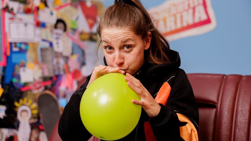 Marina checkt, wie viele Atemzüge sie benötigt, um einen Luftballon aufzupusten. – Bild: BR/​megaherz gmbh/​Hans-Florian Hopfner