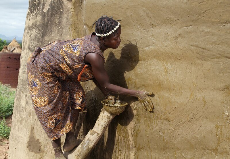Eine Frau aus dem Volk der Batammariba beim Präparieren der Lehmwand mit Kuhdung. – Bild: SWR/​Rüdiger Lorenz