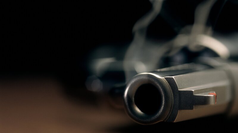 A gritty crime scene image of a smoking hand gun, revolver, lying on the floor with narrow focus on the tip if the barrel and dark background – Bild: Charles Mann/​cmannphoto