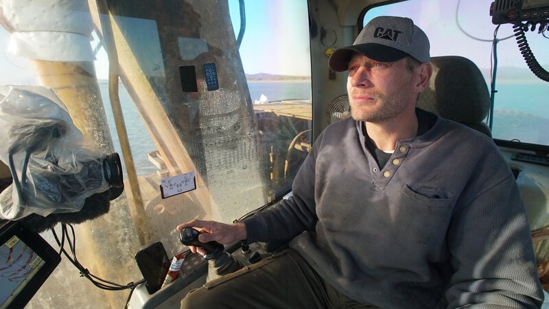 Shawn Pomrenke sits comfortably in the cabin of his excavator as he patiently looks for gold on the ocean floor. – Bild: Discovery Channel /​ Discovery Communications, LLC