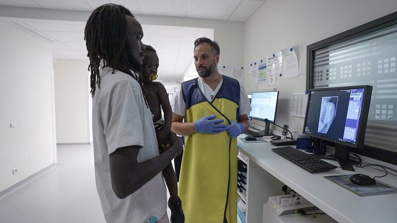 Ein Mann mit seinem Sohn spricht mit einem Arzt – Bild: Warner Bros. Discovery, Inc.