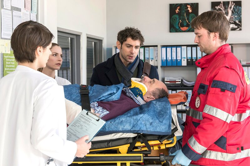 Heinz Lorbert wird in die Notaufnahme eingeliefert, nachdem er von einem Auto angefahren wurde. V.l.n.r. Dr. Theresa Koshka (Katharina Nesytowa), Julia Berger (Mirka Pigulla), Dr. Niklas Ahrend (Roy Peter Link), Heinz Lorbert (Jürgen Haug), Komparse. – Bild: HR/​ARD/​Jens Ulrich Koch