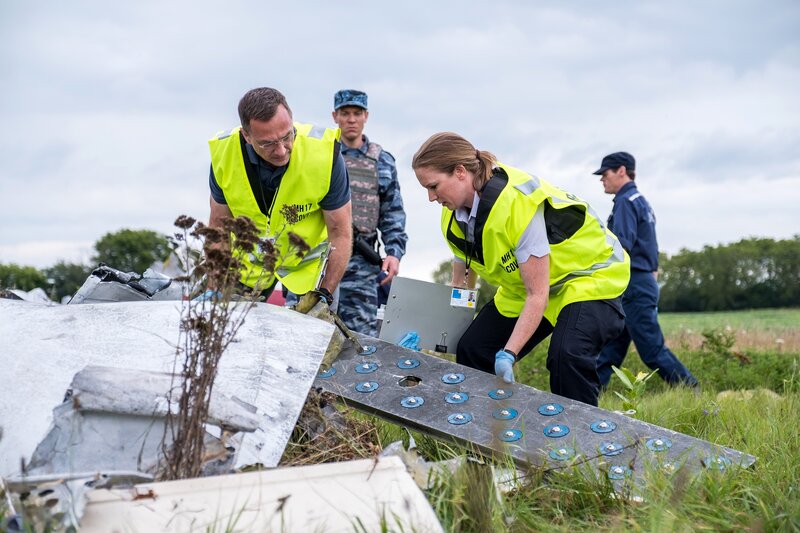 Brantford, Ontario – Die Ermittlungsassistentin (gespielt von Emily Andrews) und der Ermittler Ron Smits (gespielt von Jeff Miller) suchen an der Absturzstelle des Malaysian Airlines-Fluges 17 nach Beweisen im Wrack, während DPR-Soldaten (gespielt von Nicolas Rhind und Hintergrunddarstellern) die Absturzstelle bewachen. – Bild: PLURIMEDIA (DSG Photo /​ Darren Goldstein)