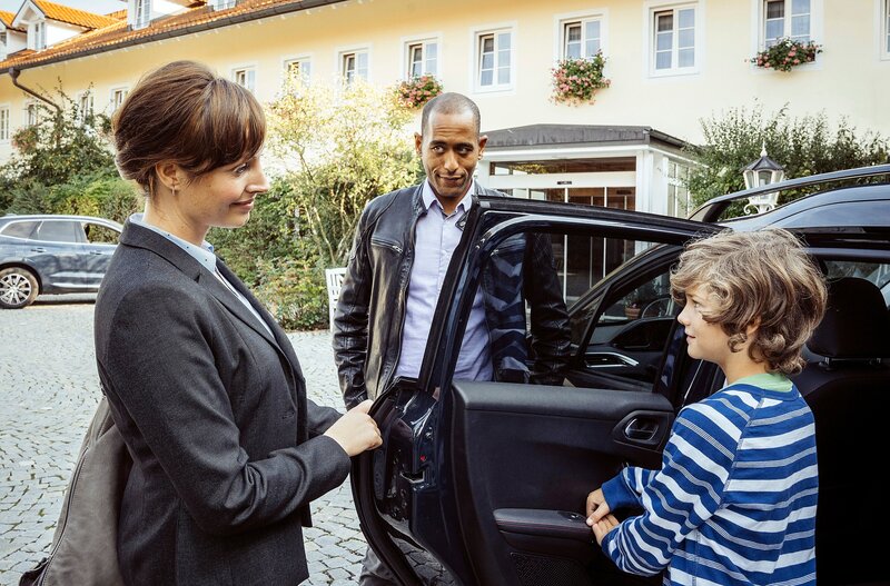Jerry Paulsen (Peter Marton, M.) spricht vor dem Gasthof zur Post mit Felicitas Beck (Dagny Dewath, l.) während ihr Sohn Florian (Anton Unertl, r.) in den Wagen steigt. – Bild: ARD/​BR/​Hendrik Heiden/​Hendrik Heiden
