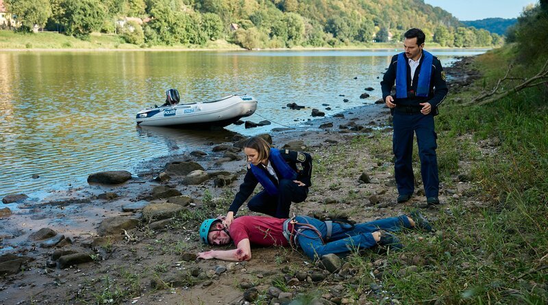 Kommissarin Macourek (Barbara Prakopenka, h.li.) kniet beim toten Kletterer. Da ist nichts mehr zu machen. Auch Kommissar Krätschmer (Ferdi Özten, re.) kommt zum Fundort, nachdem er das Boot befestigt hat. – Bild: ARD/​Rudolf Wernicke