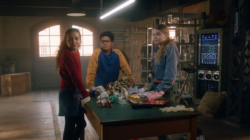 Taara (Josefine Maxima), Kofi (Mathieu Noël) und Ida wühlen sich zur Spurensicherung durch eine Tüte Müll. – Bild: NDR/​Letterbox