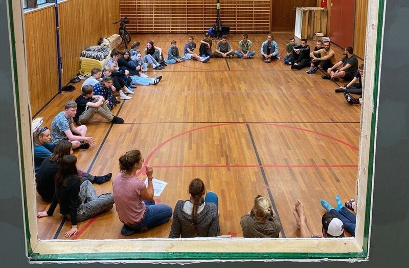 Die Tutoren des Wildnis Camps erklären den Neuankömmlingen in der Turnhalle der Schule die Pläne für die nächsten Tage. – Bild: BR/​Bewegte Zeiten Filmproduktion GmbH/​Lawrence Richards