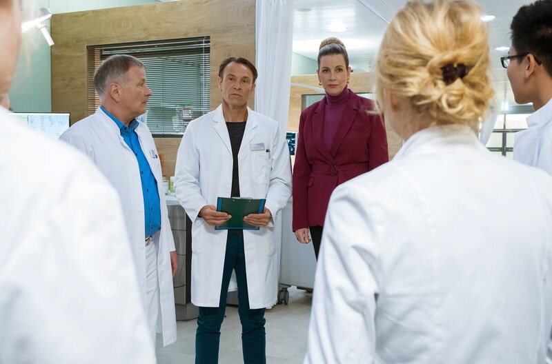Bea Hölsch (Daniela Wutte, re.) ist mit Fieber umgekippt und hat sich einen Schlüsselbeinbruch zugezogen. Ihren behandelnden Arzt Dr. Martin Stein (Bernhard Bettermann, li.) bringt sie mit ihrem sehr anschmachtenden Verhalten in eine ziemlich unangenehme Situation. Auch Dr. Kathrin Globisch (Andrea Kathrin Loewig, mi.) ist ziemlich irritiert. – Bild: MDR/​Saxonia Media/​Sebastian Kiss