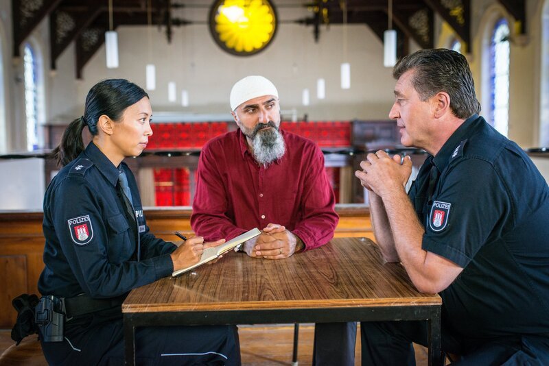 Alexa (Minh-Khai Phan-Thi, l.) und Hans (Bruno F. Apitz, r.) erfahren von Imam Adil (Yilmaz Atmaca, M.), dass auch er die Befürchtung hat, dass Mustafa im Gefängnis an die falschen Leute geraten ist. – Bild: ZDF/​Boris Laewen