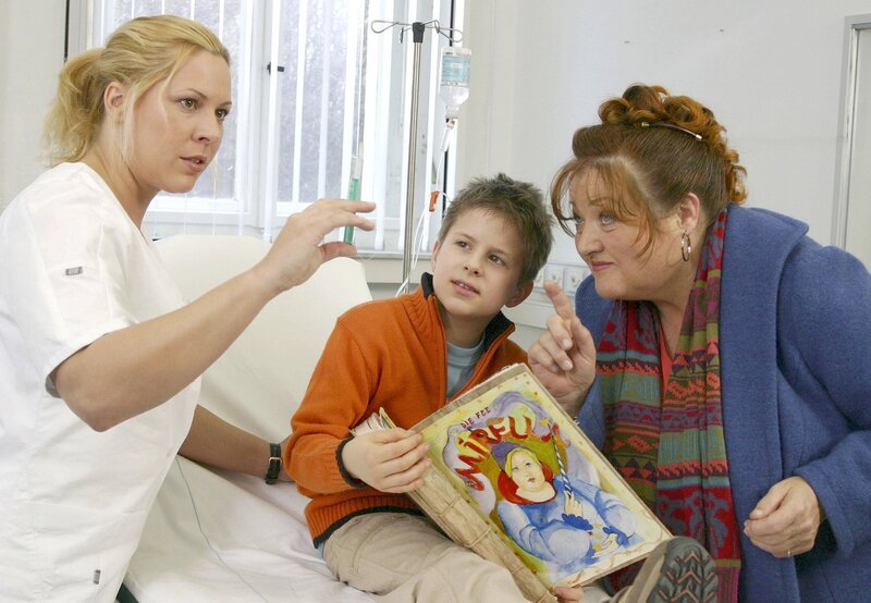 Marie (Marianne Sägebrecht, re.) lenkt den kleinen Tommy (Luka Andres) ab, damit die Krankenschwester Sonja (Nina Kapust) ihm eine Spritze geben kann. – Bild: ARD Degeto/​Sandor Domonkos