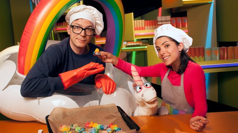 Magischer Besuch im Studio! Clarissa und Ralph bekommen in der Ah!-Küche Unterstützung von einem Einhorn. Heute gibt es nämlich Einhornhaufen. Ja, das was beim Einhorn hinten raus kommt, ist gar nicht eklig, sondern sehr schön bunt und zuckersüß. Und wie man Einhornhaufen auch ohne ein eigenes Einhorn herstellen kann, zeigen Clarissa und Ralph während sie sich z.B. diesem bunten Thema der Sendung widmen. Kann man bis zum Ende des Regenbogens oder in ihn hineinlaufen? – Bild: WDR/​Thorsten Schneider