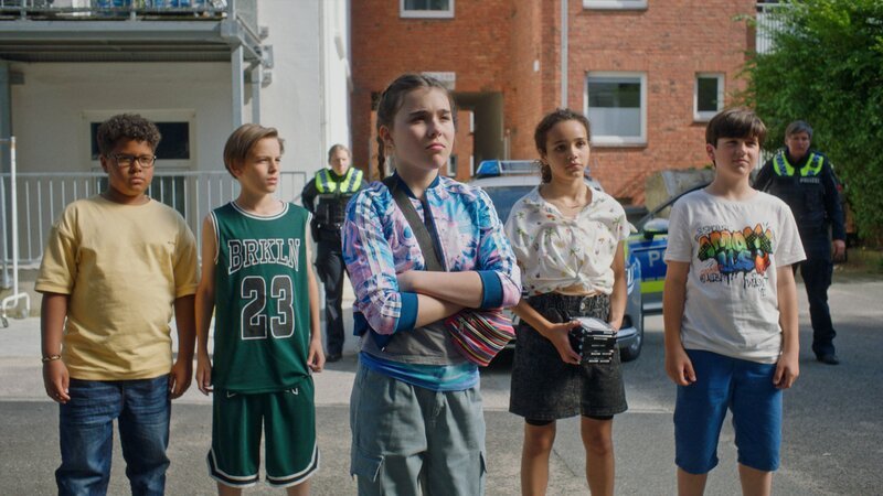 Emma (Lucy Korsus, Mitte) wird von den Pfefferkörnern unterstützt, als sie vor dem Täter steht und ihn identifizieren soll. – Bild: NDR/​Letterbox